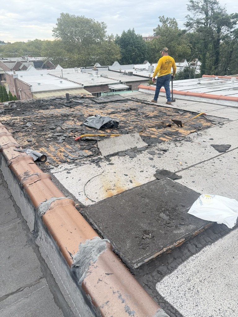 MLM Construction Group roofer stripping a failed flat roof section down to the deck in Brooklyn