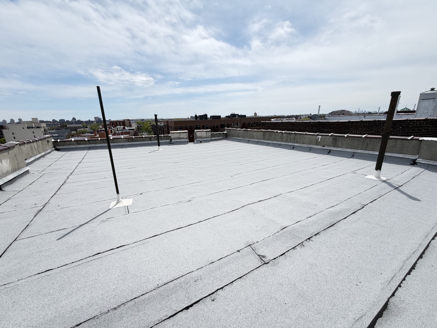 Brooklyn flat roof with parapet walls on three sides and exposed pipe penetrations